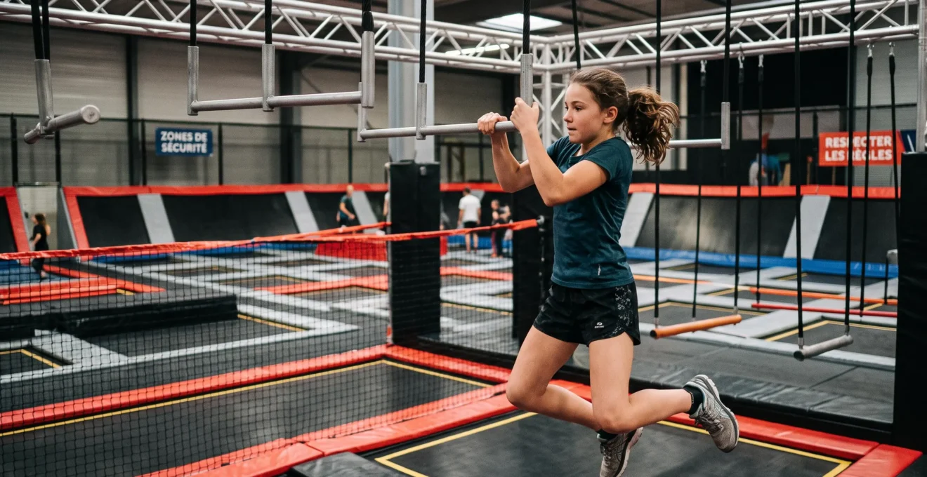 Pré-adolescent d'environ 11-13 ans en train de franchir un obstacle sur un parcours Ninja Warrior suspendu au-dessus de trampolines de sécurité